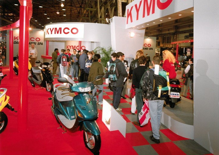 1993年官方正式參展的攤位實景圖。1992年，光陽與本田正式結束合作關係，改用自創的「KYMCO」品牌行銷國際迄今達108國，全球累計銷售超過千萬台KYMCO機車，從東京的街頭、義大利米蘭到巴黎香榭大道，甚至在非洲塞內加爾的沙漠，都可見到KYMCO的身影，在台目前連續20年第一、歐洲在義大利、西班牙都名列前三大品牌。2.jpg